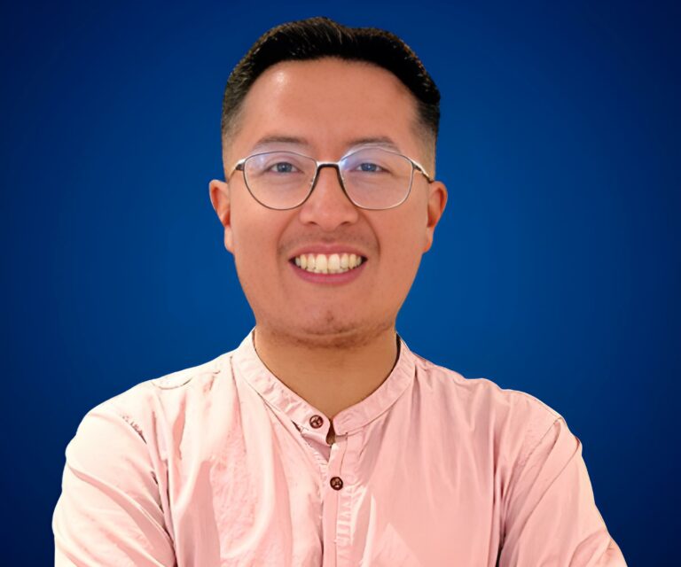 Jaime Vaca Guzmán con camisa rosa, sonriendo frente a un fondo azul