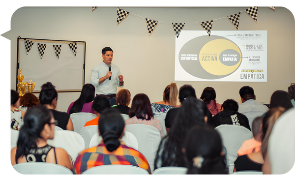 Pablo Hurtado dando una conferencia sobre comunicación empática, con una audiencia atenta. En la pantalla se proyecta un diagrama explicativo sobre los niveles de escucha y empatía.